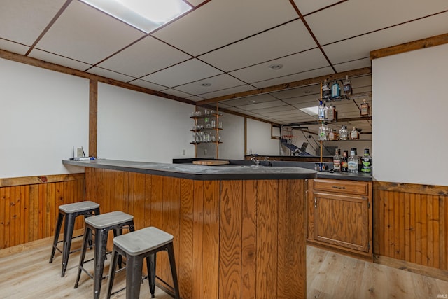 bar featuring wood walls, a drop ceiling, and light wood-type flooring