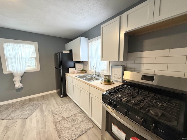 kitchen featuring gas range, sink, light hardwood / wood-style flooring, decorative backsplash, and white cabinets