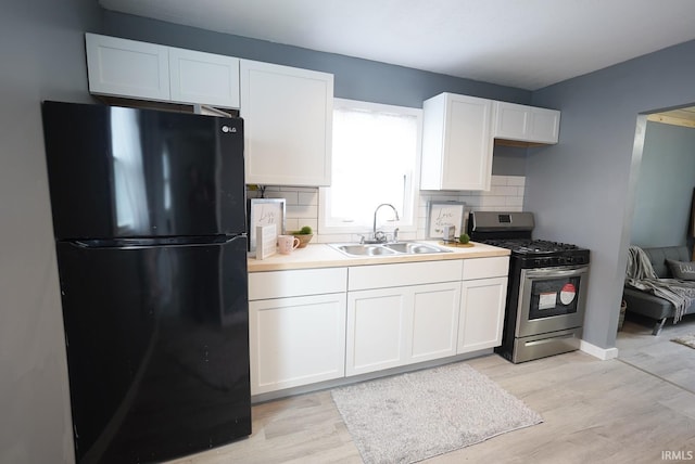 kitchen featuring backsplash, black fridge, sink, stainless steel gas stove, and white cabinetry