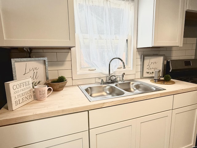 kitchen with white cabinetry, decorative backsplash, sink, and range