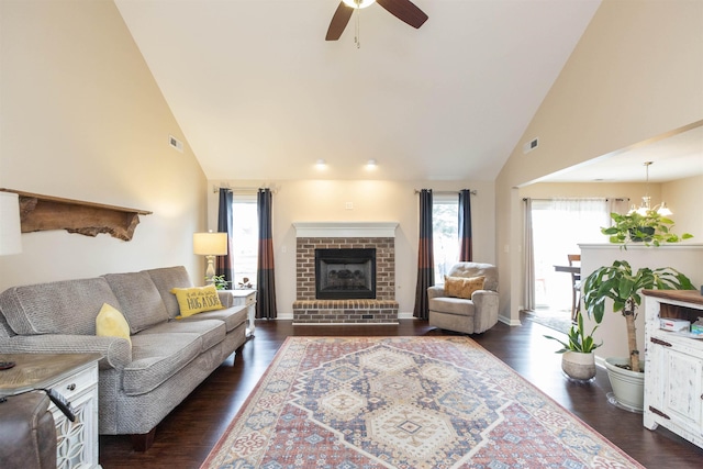 living room featuring dark hardwood / wood-style floors, ceiling fan with notable chandelier, high vaulted ceiling, and a brick fireplace