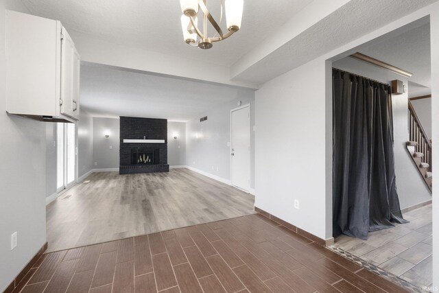 unfurnished living room featuring a notable chandelier, wood-type flooring, a textured ceiling, and a brick fireplace