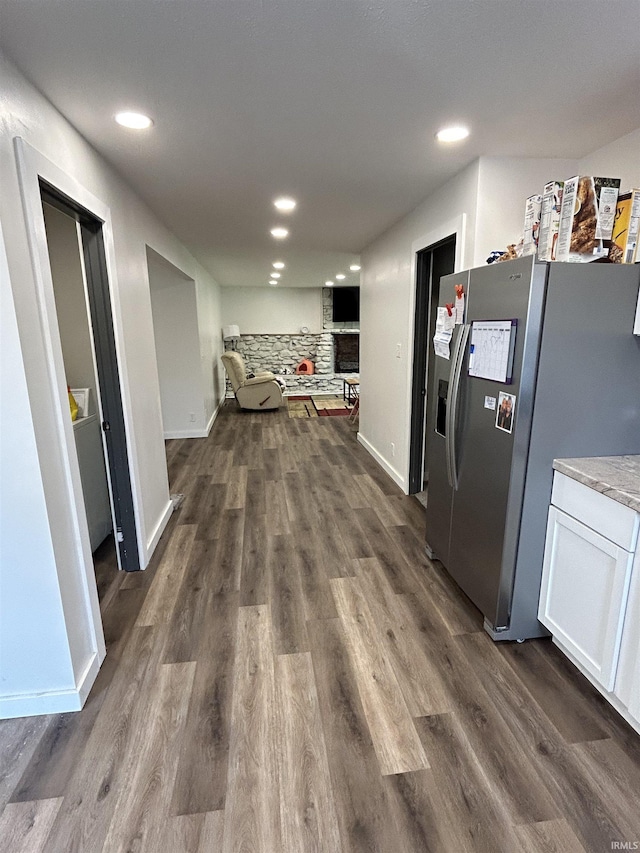 kitchen featuring white cabinets, stainless steel fridge with ice dispenser, a large fireplace, and dark wood-type flooring