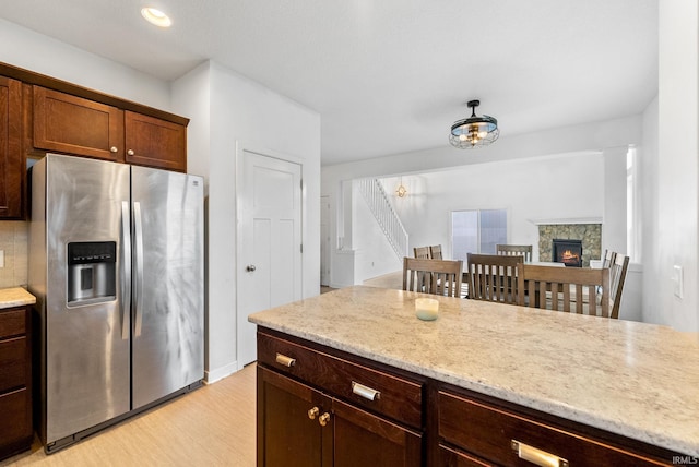 kitchen featuring decorative backsplash, stainless steel fridge, light wood-type flooring, light stone countertops, and a stone fireplace