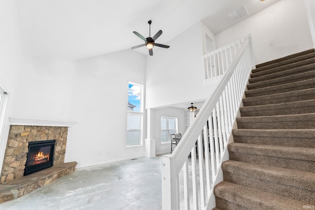 staircase with concrete flooring, high vaulted ceiling, ceiling fan, and a fireplace