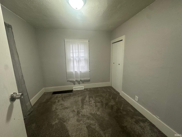 spare room with a textured ceiling and dark colored carpet