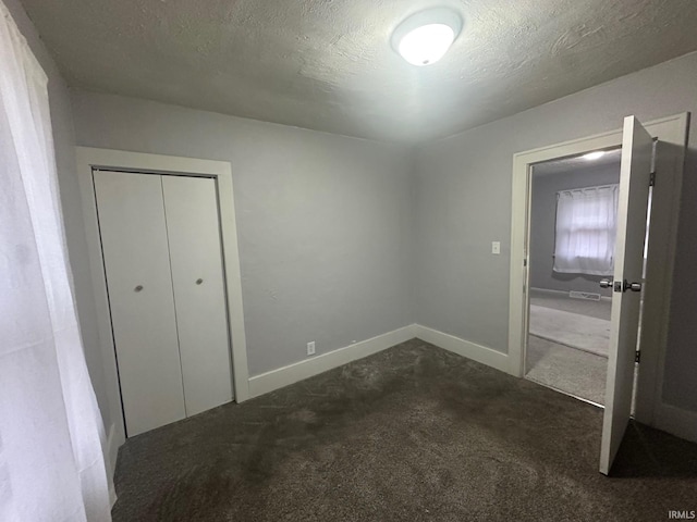 unfurnished bedroom with dark carpet, a textured ceiling, and a closet