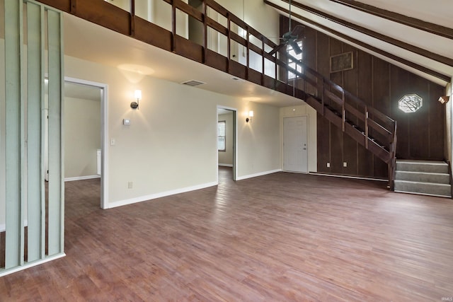 unfurnished living room featuring beam ceiling, dark hardwood / wood-style floors, high vaulted ceiling, and wood walls