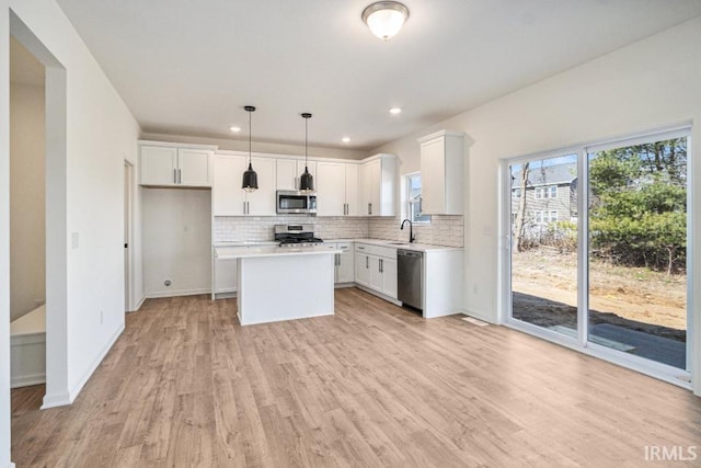 kitchen with a center island, sink, hanging light fixtures, stainless steel appliances, and white cabinets