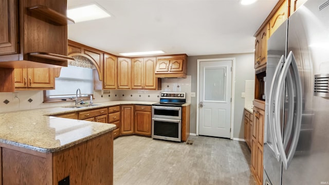 kitchen with light stone countertops, sink, light hardwood / wood-style flooring, kitchen peninsula, and appliances with stainless steel finishes