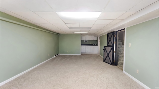 basement with a paneled ceiling, light colored carpet, and baseboard heating