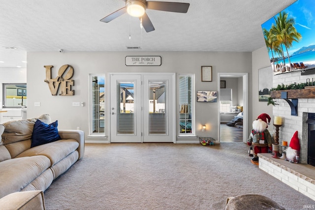 carpeted living room featuring ceiling fan, a healthy amount of sunlight, a textured ceiling, and a brick fireplace