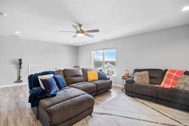 living room featuring ceiling fan, light hardwood / wood-style floors, and a textured ceiling