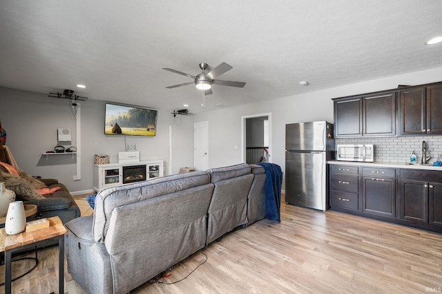 living room featuring ceiling fan, sink, a textured ceiling, a fireplace, and light wood-type flooring