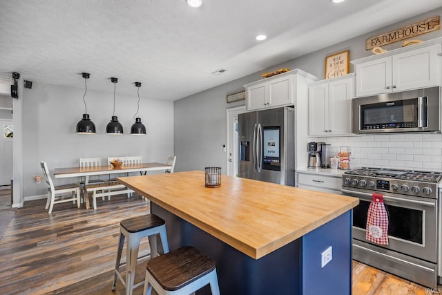 kitchen with dark hardwood / wood-style flooring, white cabinets, a kitchen island, and appliances with stainless steel finishes