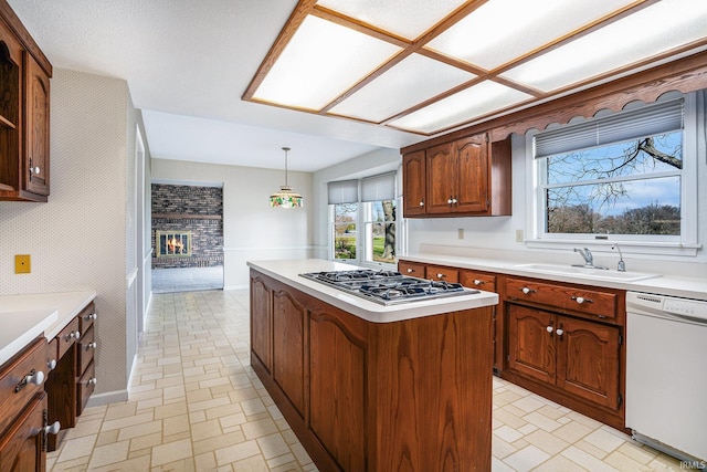 kitchen with dishwasher, a center island, sink, a brick fireplace, and stainless steel gas cooktop