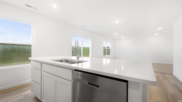 kitchen featuring a kitchen island with sink, white cabinets, sink, stainless steel dishwasher, and light wood-type flooring