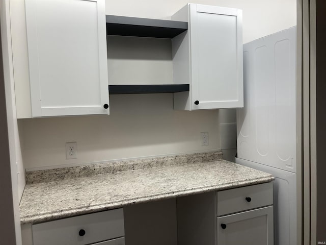 kitchen with light stone countertops, built in desk, and white cabinetry