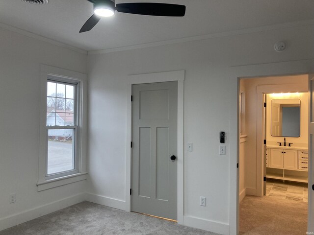 unfurnished bedroom featuring sink, ensuite bath, ceiling fan, ornamental molding, and light colored carpet