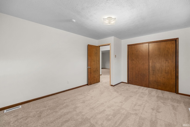 unfurnished bedroom featuring light colored carpet, a textured ceiling, and a closet