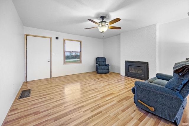 living room with ceiling fan, a large fireplace, and light hardwood / wood-style flooring