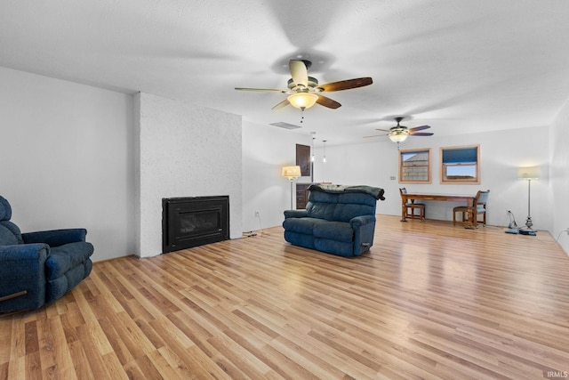 living room with a textured ceiling, ceiling fan, light wood-type flooring, and a fireplace