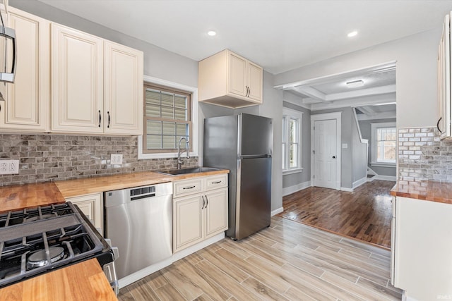 kitchen featuring wood counters, sink, light wood-type flooring, beam ceiling, and stainless steel appliances