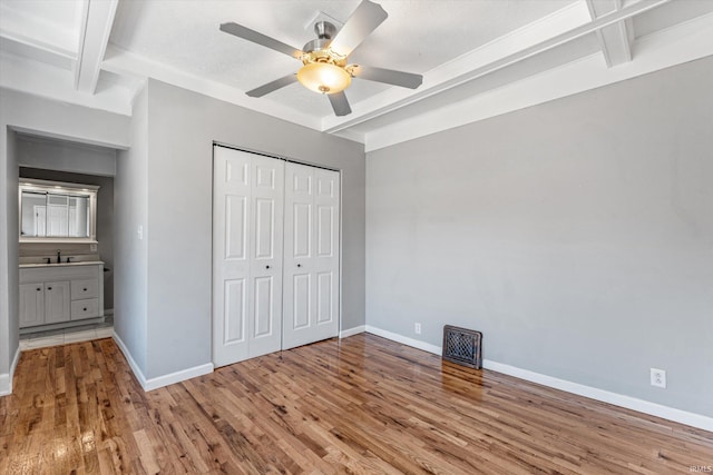 unfurnished bedroom with ceiling fan, beamed ceiling, and light hardwood / wood-style floors