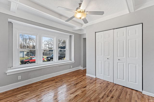 unfurnished bedroom featuring a textured ceiling, ceiling fan, hardwood / wood-style flooring, beamed ceiling, and a closet