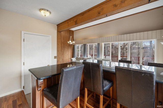 kitchen with a breakfast bar area, wood walls, a chandelier, and wood-type flooring