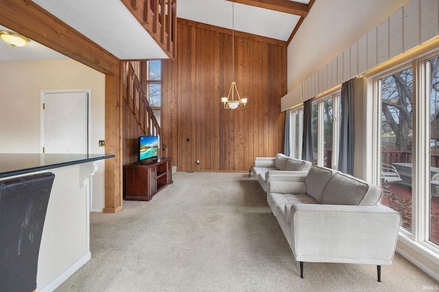 carpeted living room with beamed ceiling, wooden walls, high vaulted ceiling, and a notable chandelier