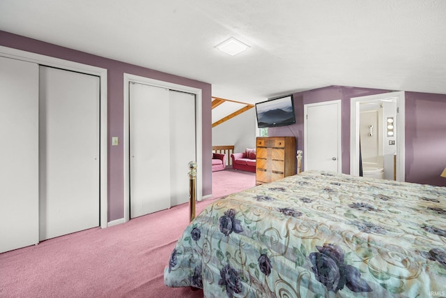 carpeted bedroom featuring connected bathroom, two closets, and vaulted ceiling