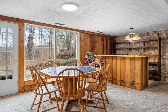 dining area featuring wood walls, carpet, and a textured ceiling