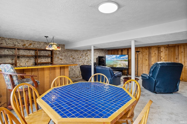 dining area with bar area, wooden walls, carpet floors, and a textured ceiling