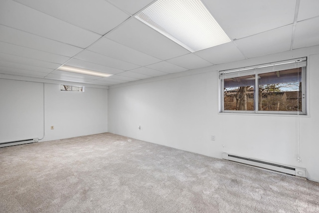 carpeted empty room featuring a paneled ceiling and a baseboard heating unit