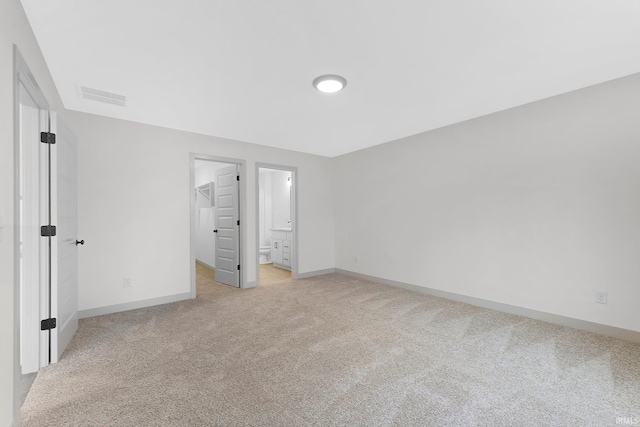 unfurnished bedroom with light colored carpet, ensuite bath, and a walk in closet