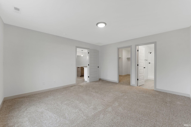 unfurnished bedroom with a spacious closet, light colored carpet, ensuite bath, and a closet