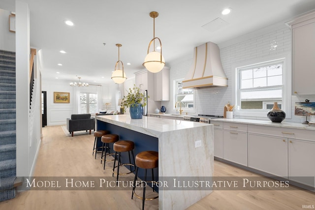 kitchen featuring decorative light fixtures, a kitchen island, premium range hood, and light hardwood / wood-style flooring