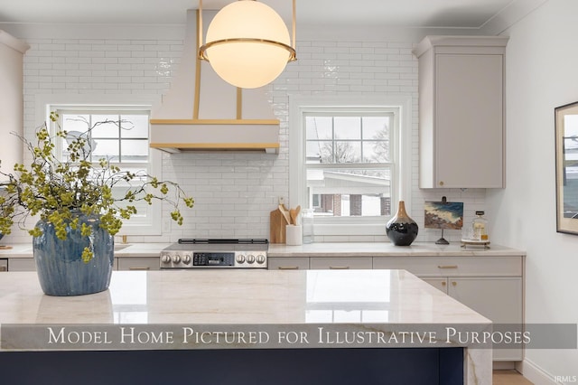 kitchen with hanging light fixtures, light stone counters, backsplash, premium range hood, and stainless steel stove