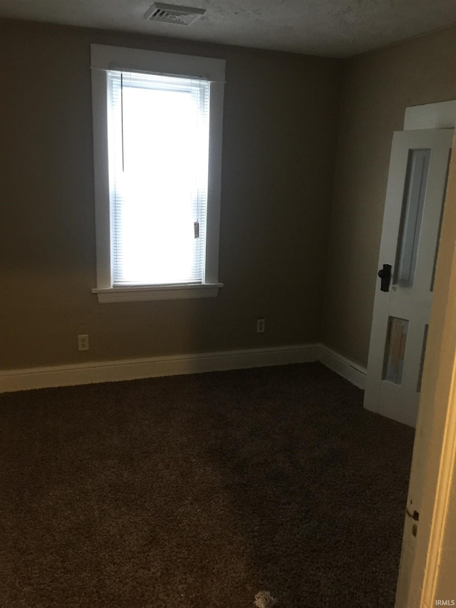 spare room featuring dark carpet and a textured ceiling