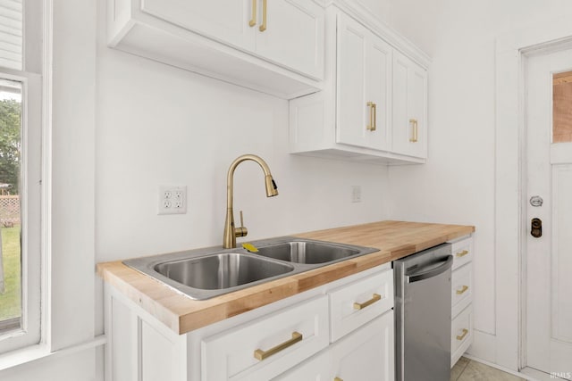 kitchen featuring wood counters, stainless steel dishwasher, sink, light tile patterned floors, and white cabinetry