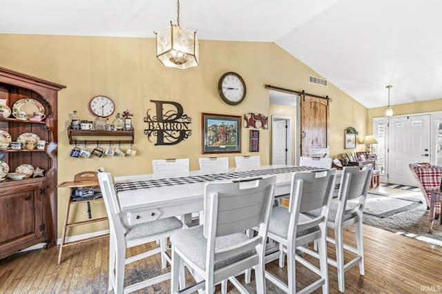 dining space with a barn door, wood-type flooring, and vaulted ceiling