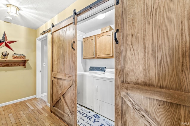 washroom featuring cabinets, light wood-type flooring, a textured ceiling, washer and dryer, and a barn door