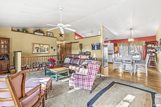 living room featuring hardwood / wood-style floors, ceiling fan, a barn door, and vaulted ceiling