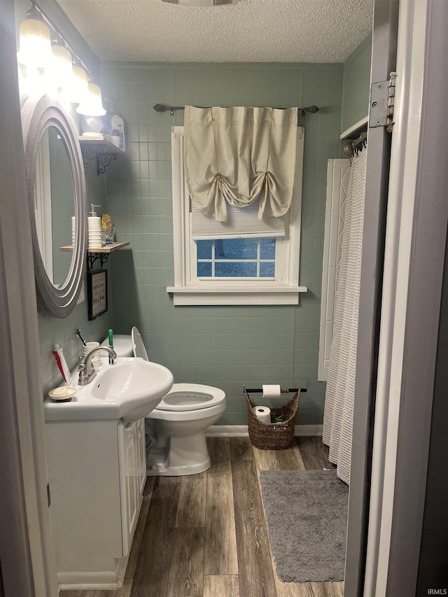 bathroom with a textured ceiling, vanity, wood-type flooring, and tile walls