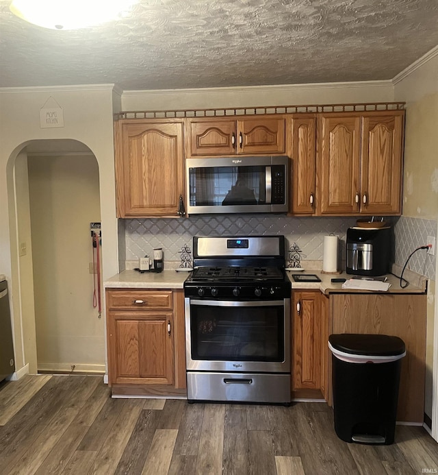 kitchen featuring ornamental molding, a textured ceiling, tasteful backsplash, dark hardwood / wood-style flooring, and stainless steel appliances