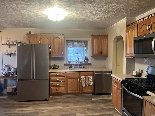 kitchen with hardwood / wood-style floors, backsplash, sink, ornamental molding, and appliances with stainless steel finishes