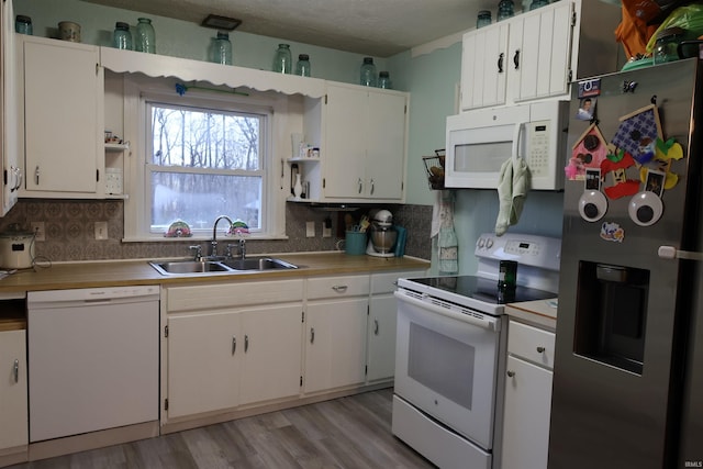 kitchen featuring white appliances, sink, light wood-type flooring, tasteful backsplash, and white cabinetry