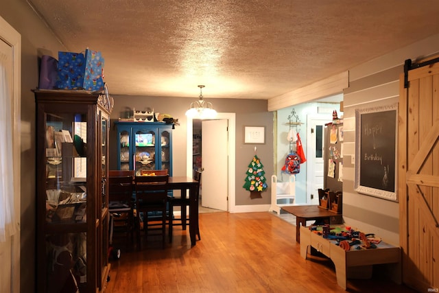 dining area featuring a barn door, a chandelier, a textured ceiling, and hardwood / wood-style flooring