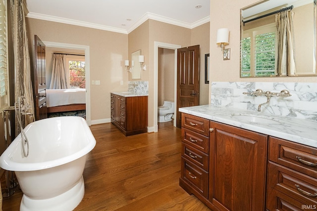 bathroom featuring ornamental molding, a washtub, vanity, wood-type flooring, and toilet